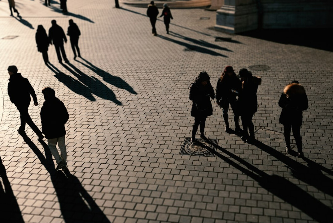 Anonyme Silhouetten von Menschen, die in der Abenddämmerung einen Platz überqueren